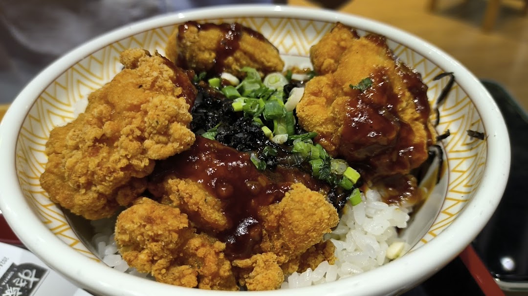 A close-up of a bowl of crispy fried chicken (karaage) with sauce, rice, and green onions.