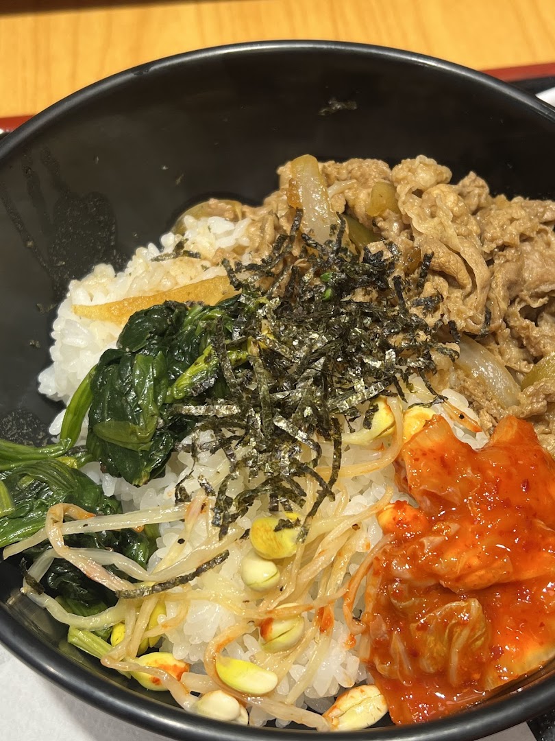 A close-up of a delicious Sukiya rice bowl featuring beef, vegetables, and kimchi.