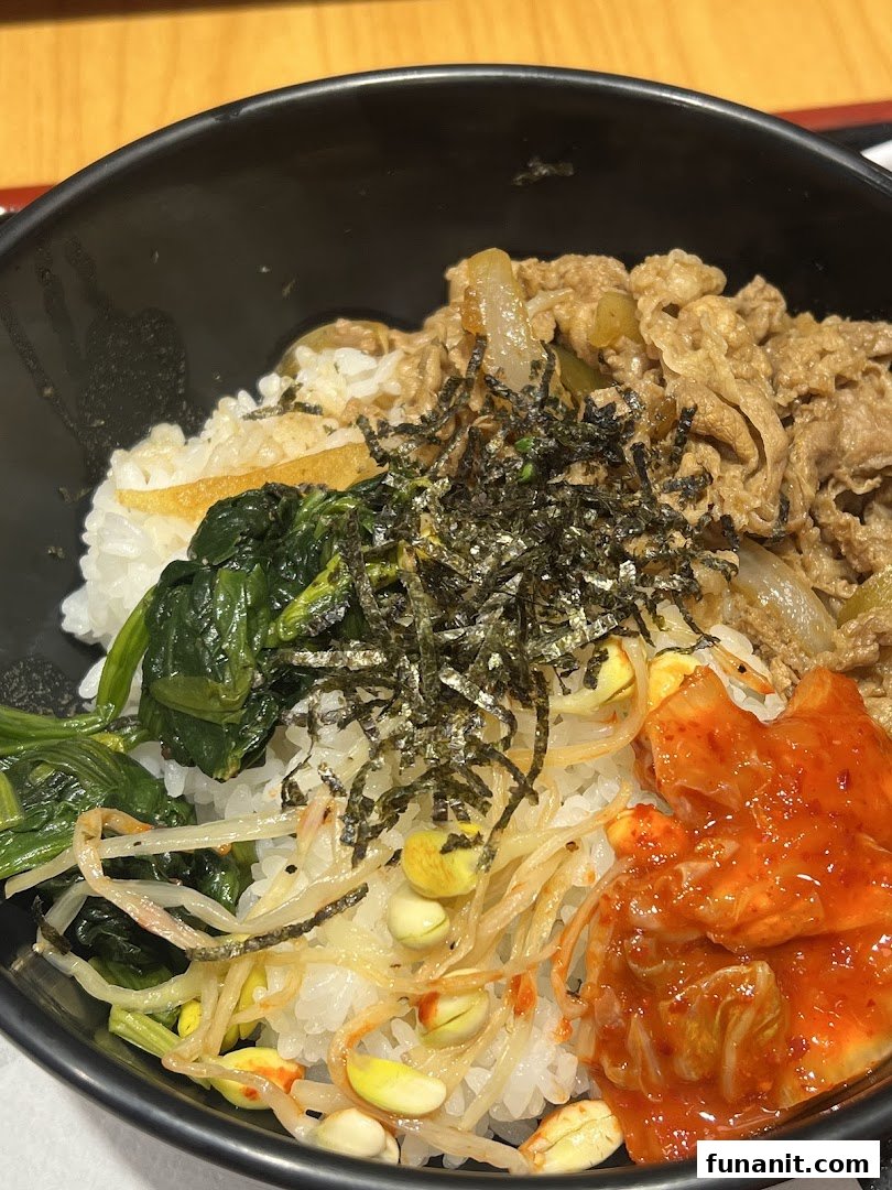 A close-up of a delicious Sukiya rice bowl featuring beef, vegetables, and kimchi.