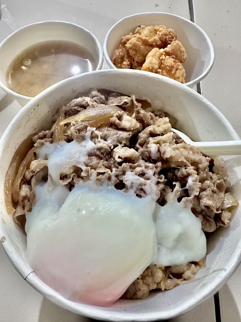 A close-up of Sukiya's signature gyudon with a poached egg, served with fried chicken and soup.