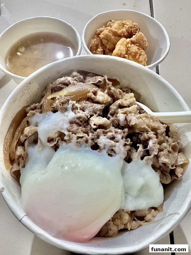 A close-up of Sukiya's signature gyudon with a poached egg, served with fried chicken and soup.