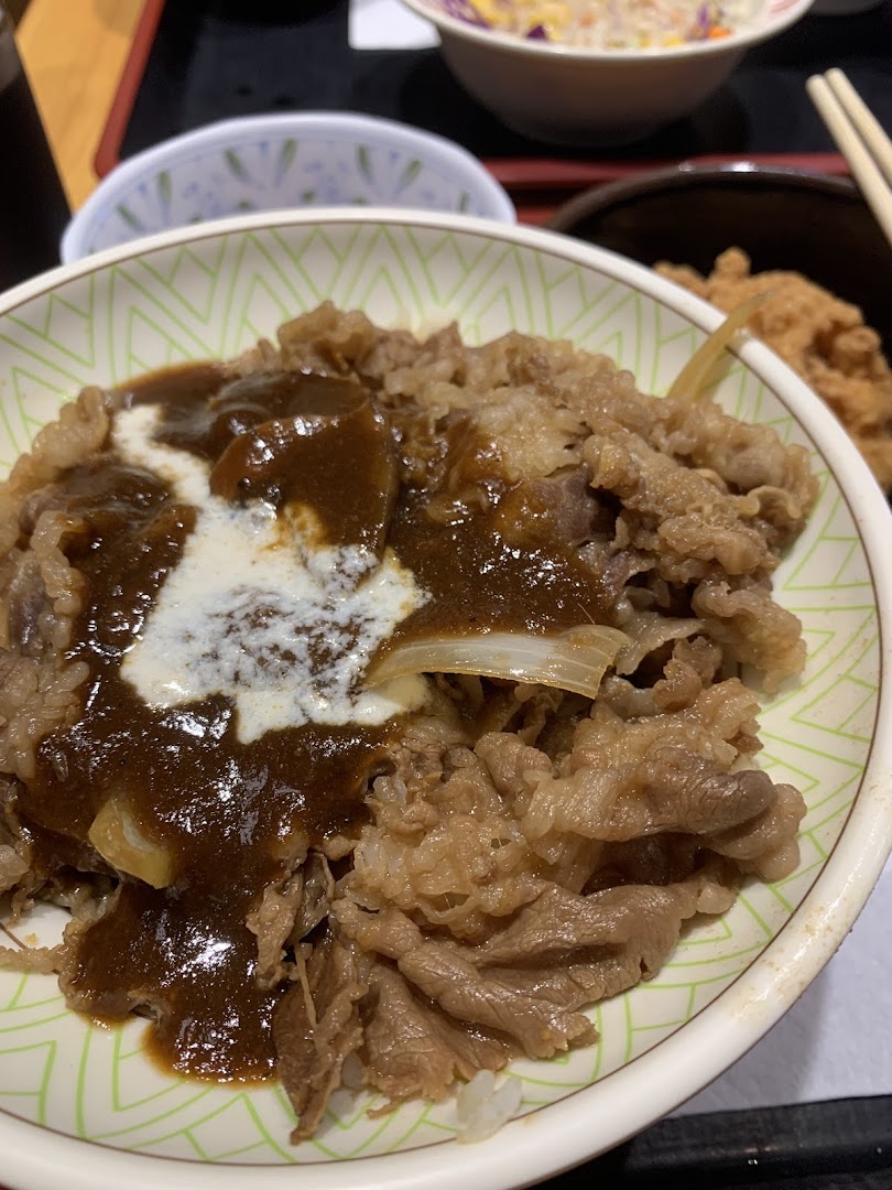 A close-up of a delicious Sukiya Gyudon bowl topped with curry and cream sauce.