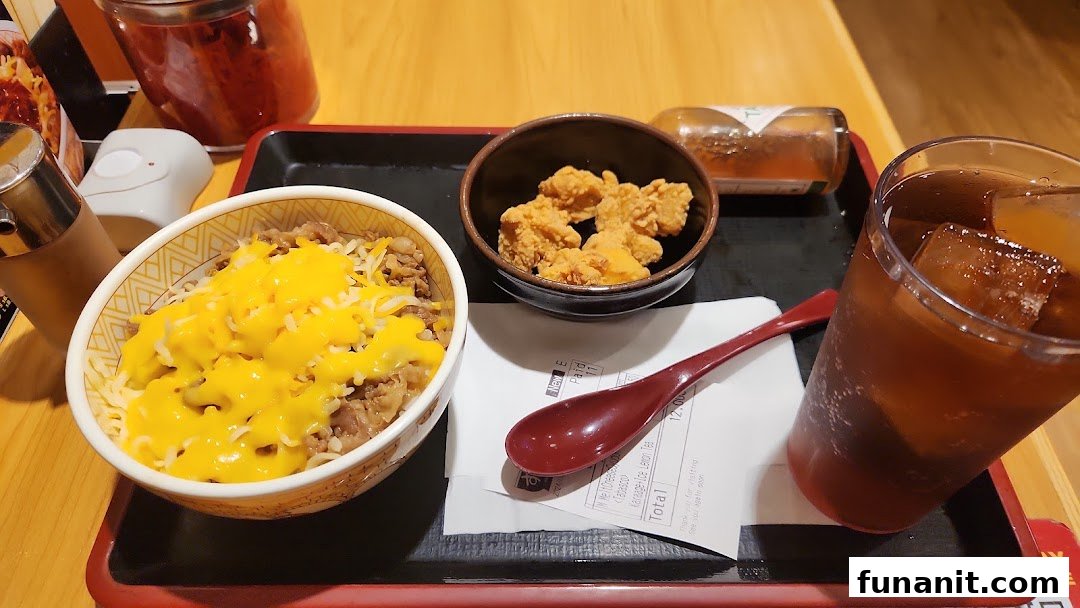 A delicious Sukiya meal featuring cheesy gyudon, crispy karaage, and refreshing iced tea on a tray.