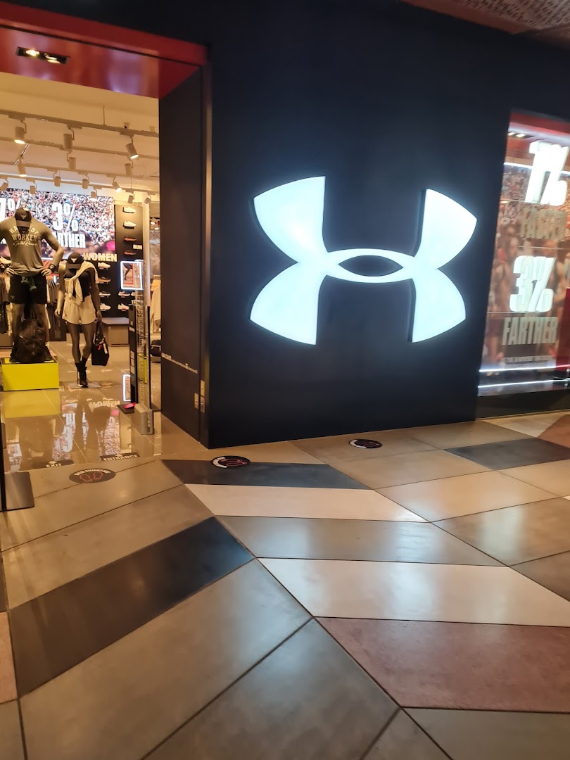 The entrance of an Under Armour store featuring its prominent glowing logo and mannequins inside.