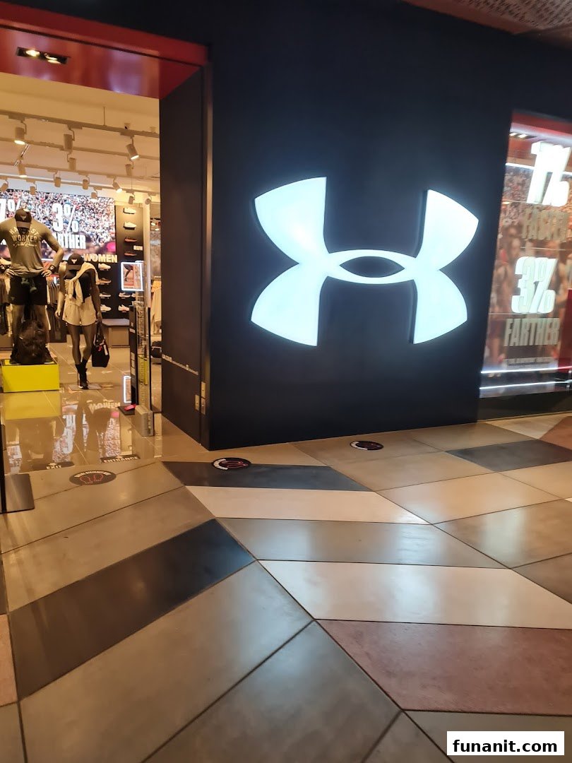 The entrance of an Under Armour store featuring its prominent glowing logo and mannequins inside.