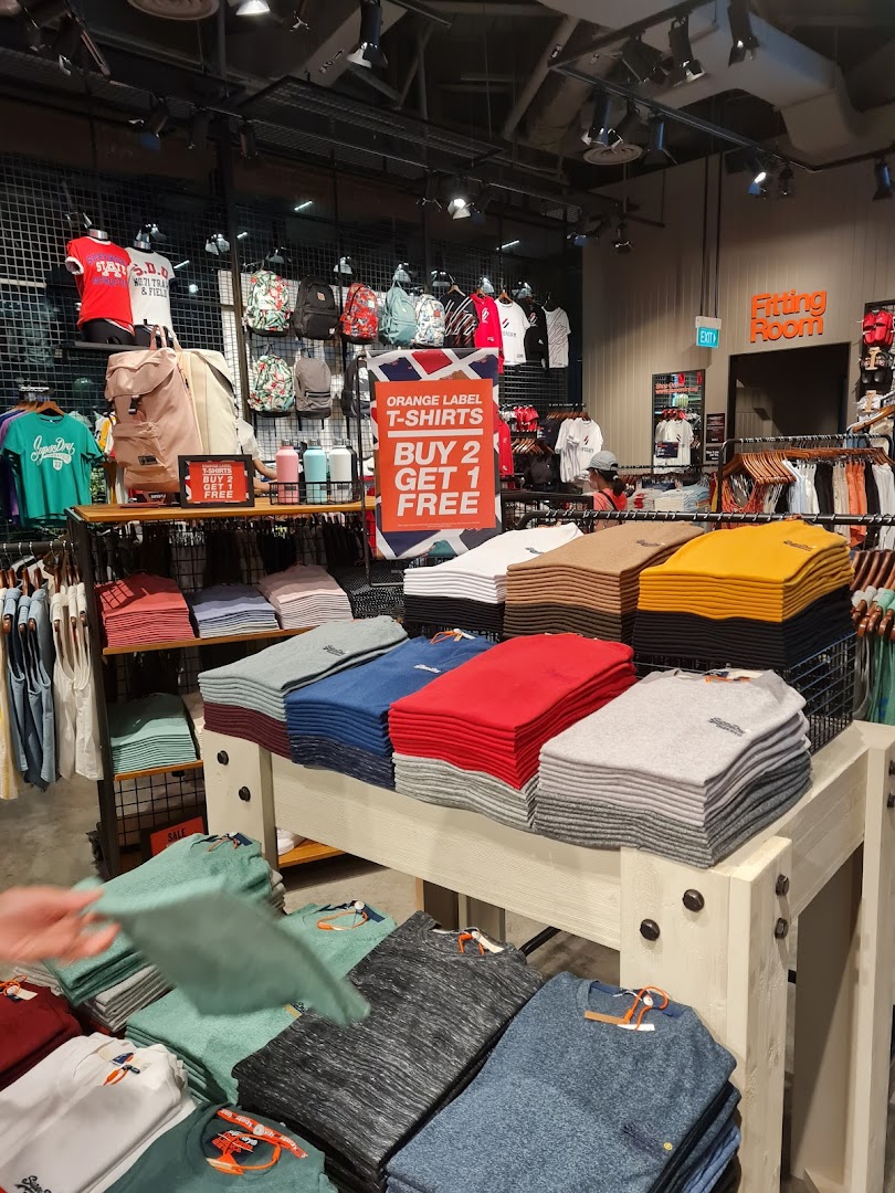 Interior view of a Superdry store showcasing folded apparel, backpacks, and a 'Buy 2 Get 1 Free' T-shirt offer.