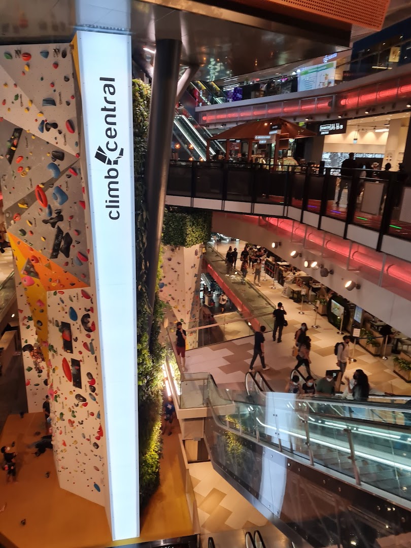 A vibrant multi-level mall interior featuring a large indoor climbing wall and shoppers.