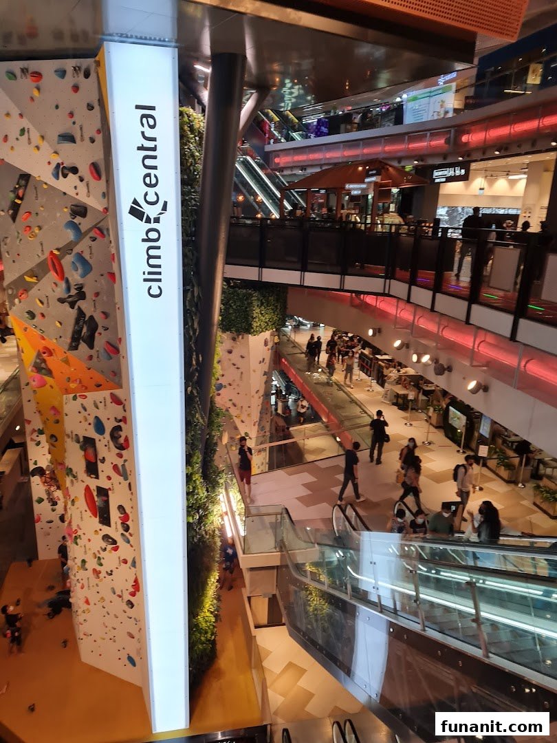 A vibrant multi-level mall interior featuring a large indoor climbing wall and shoppers.