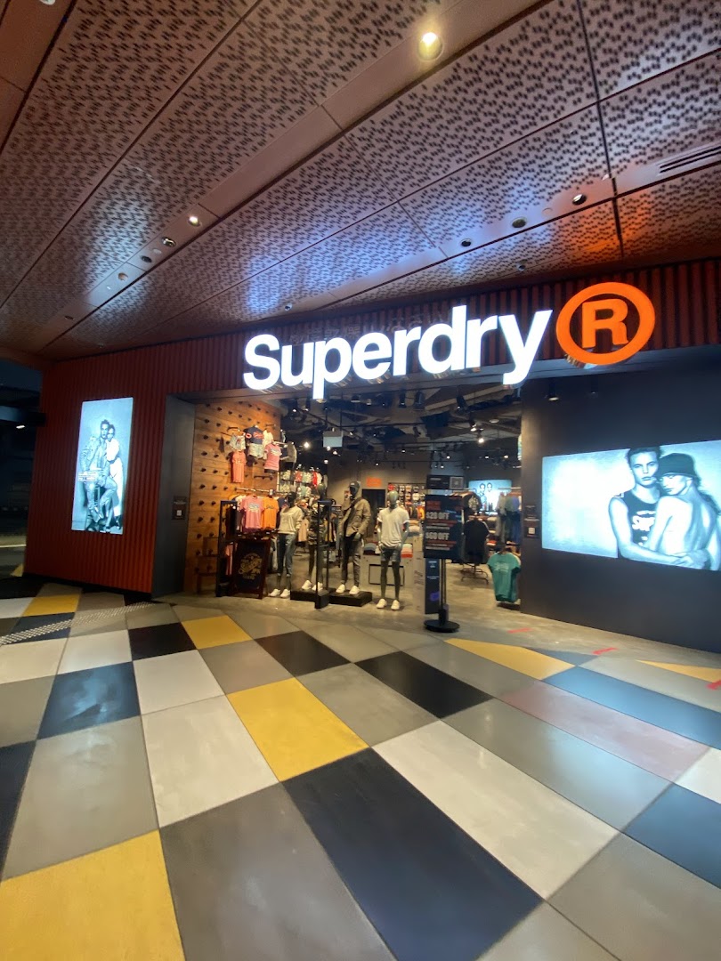 The Superdry shop entrance featuring its illuminated logo, mannequins, and promotional displays.