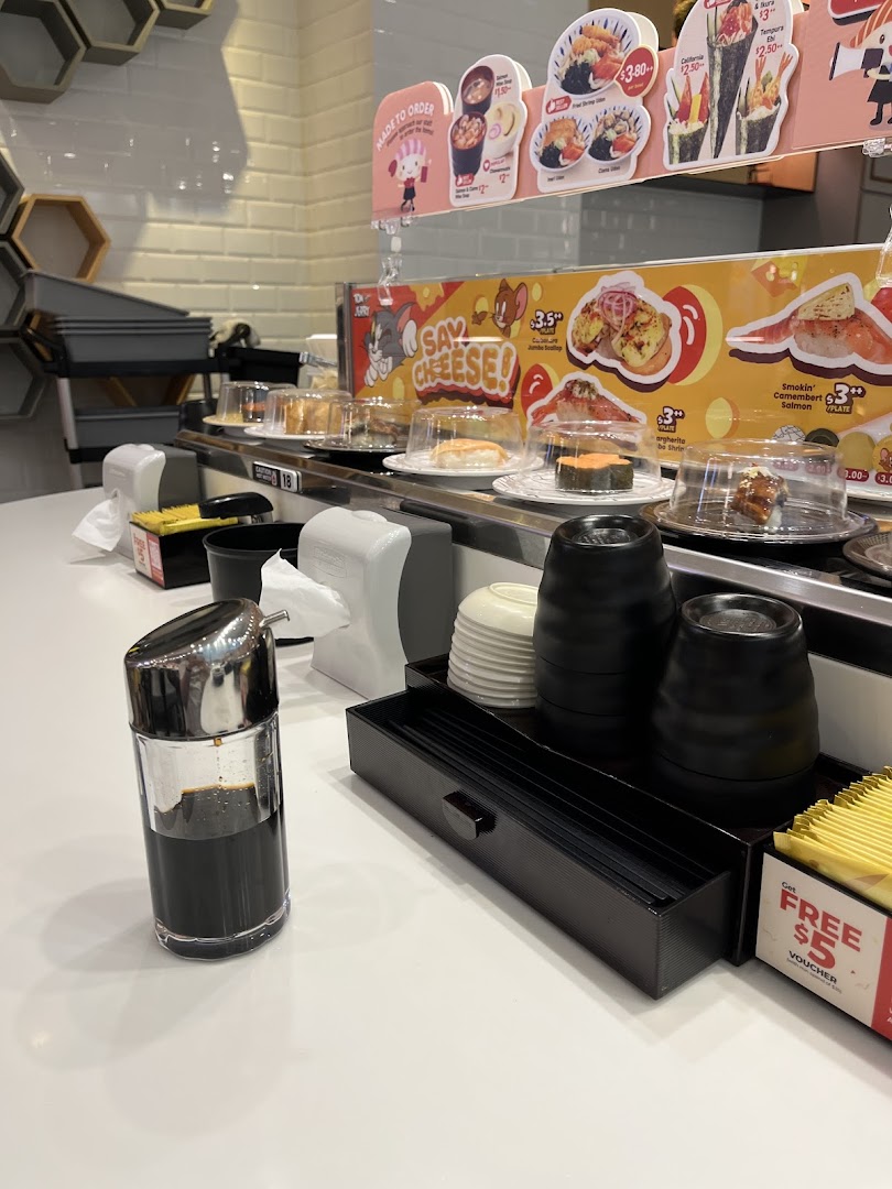 A close-up view of a sushi conveyor belt with various plates, condiments, and promotional signs.
