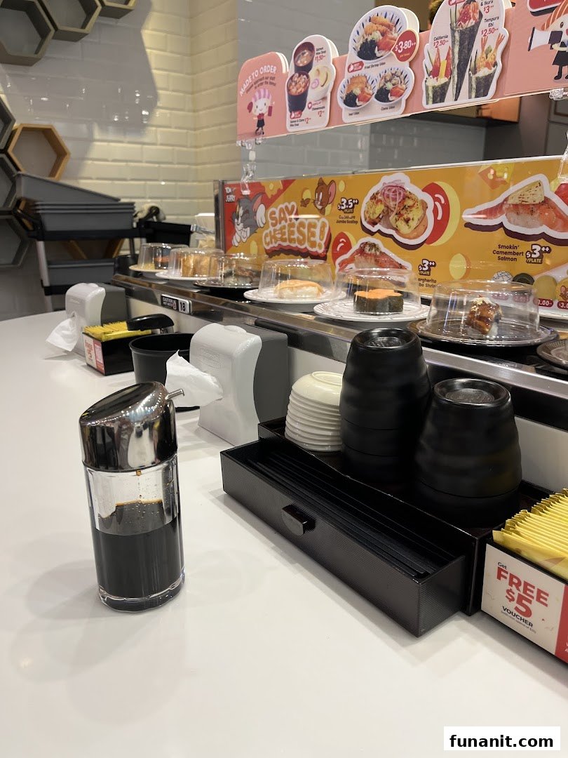 A close-up view of a sushi conveyor belt with various plates, condiments, and promotional signs.