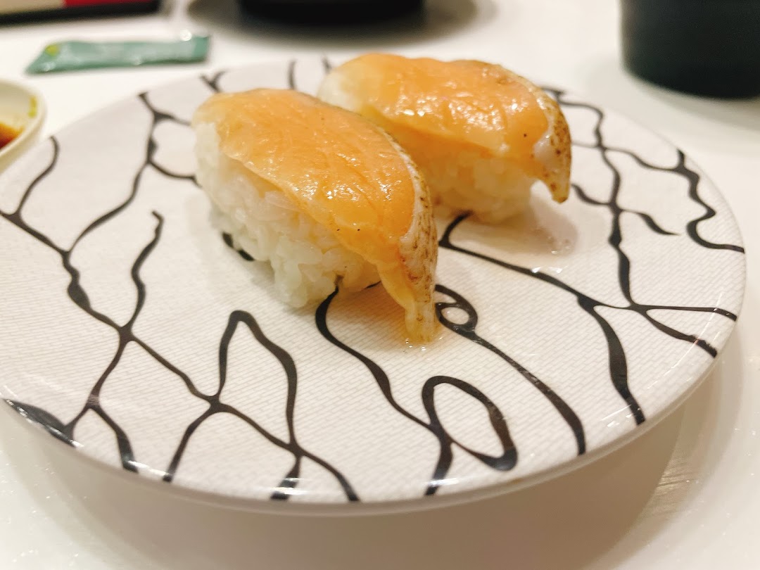 Two pieces of fresh salmon sushi elegantly presented on a patterned white plate.