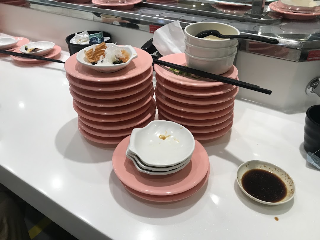 Stacks of used pink plates and bowls on a white counter at a busy sushi restaurant.