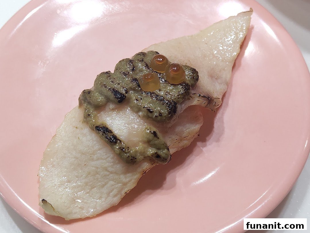 A close-up of a piece of sushi with a green topping and orange roe on a pink plate.