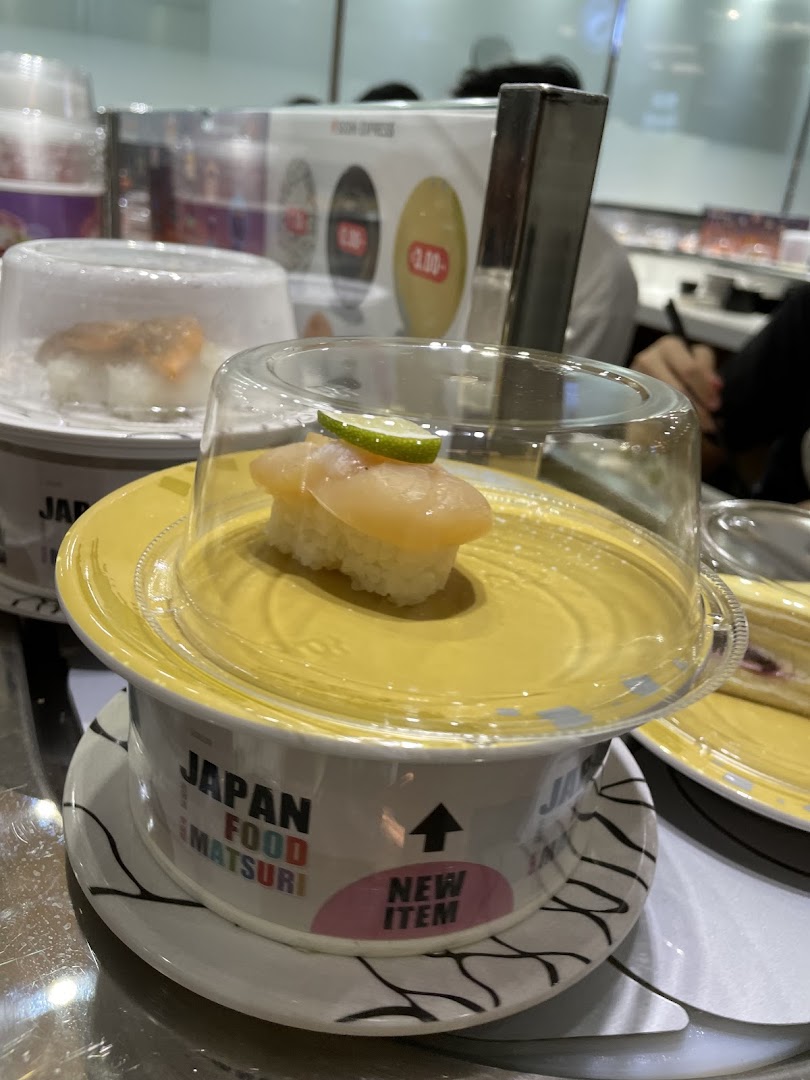 Sushi plates with covers on a conveyor belt at Sushi Express, featuring a new item.