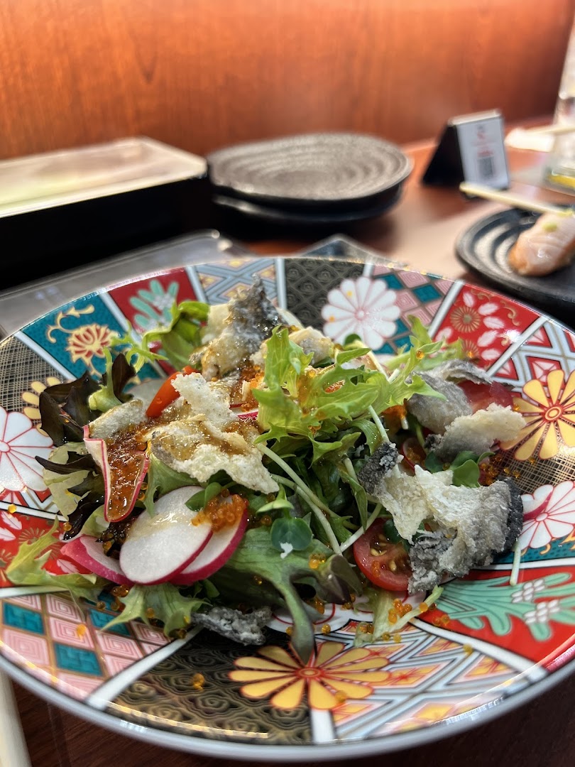 A vibrant salad with crispy fish skin, fresh greens, and roe, served on a decorative Japanese plate.