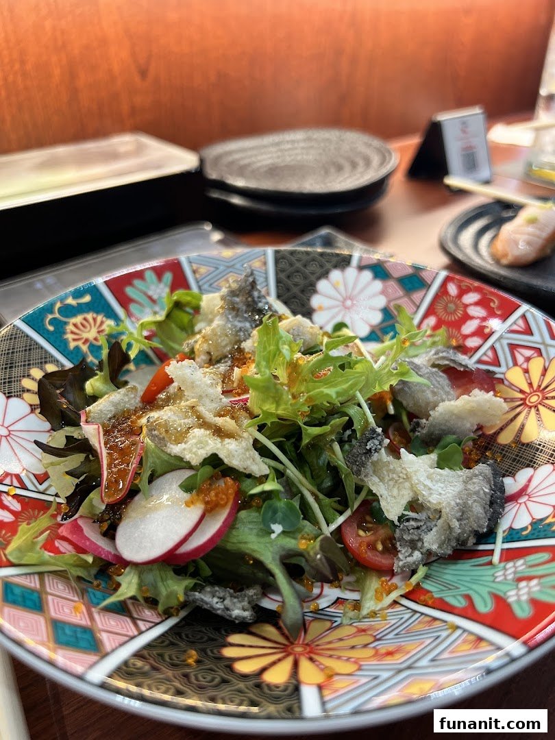A vibrant salad with crispy fish skin, fresh greens, and roe, served on a decorative Japanese plate.