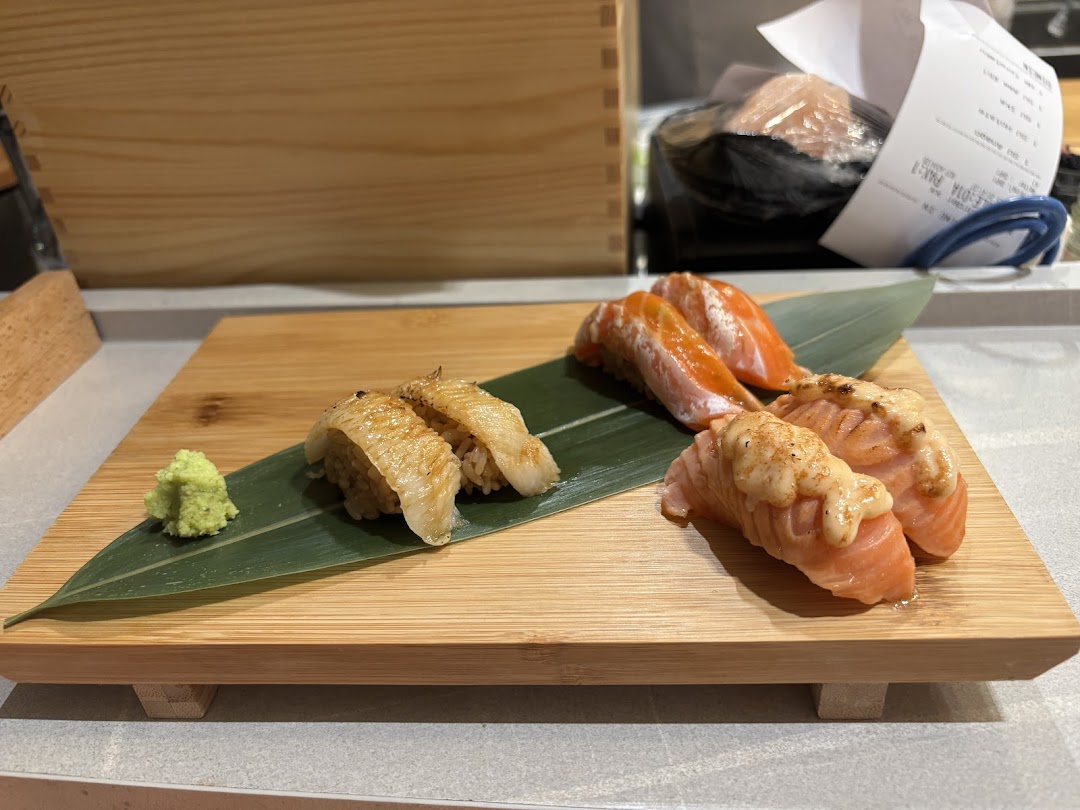 Assorted sushi pieces, including salmon and possibly eel, served on a wooden board with wasabi.