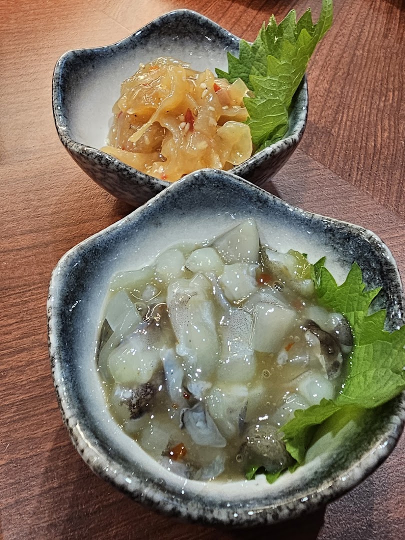 Two small bowls of traditional Japanese appetizers, featuring seasoned jellyfish and squid, served on a wooden table.