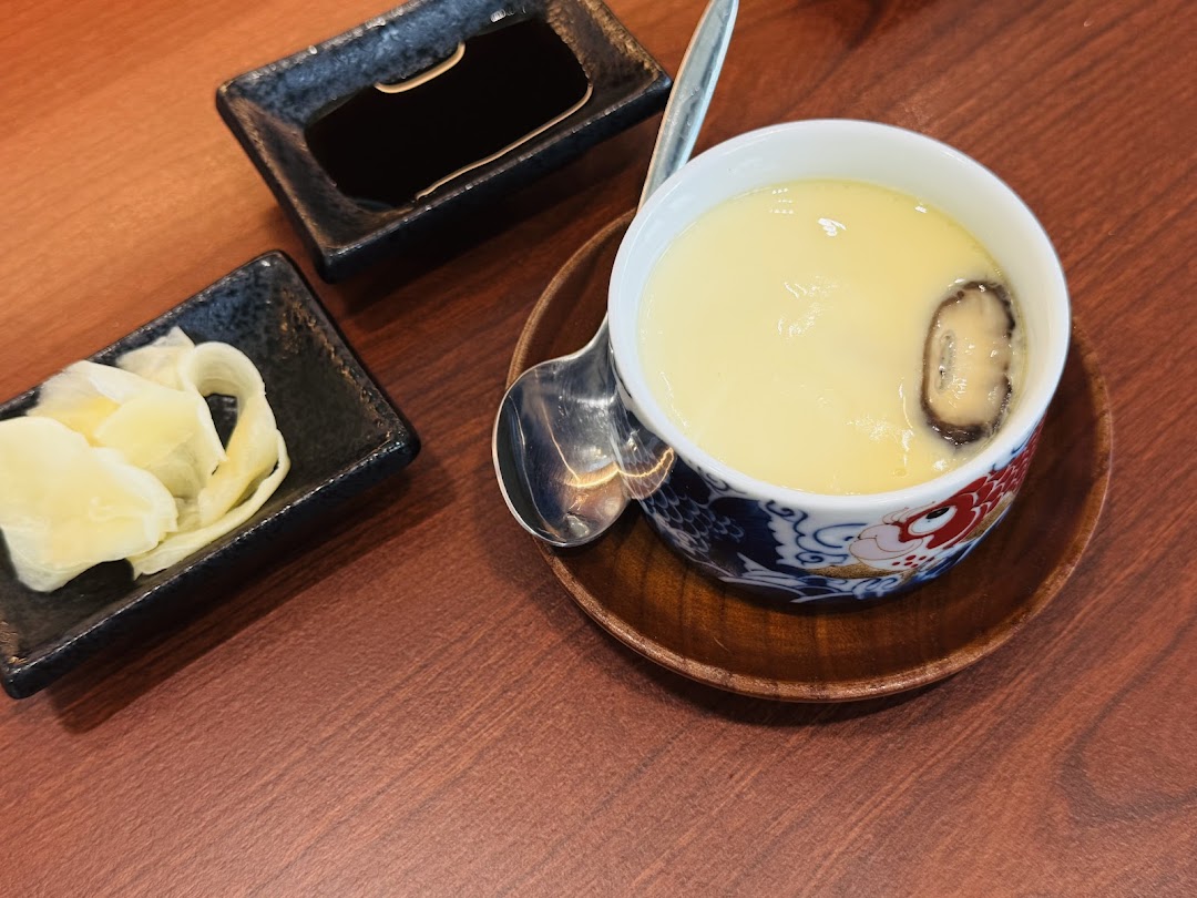 A close-up of a steaming Chawanmushi (savory egg custard) served with pickled ginger and soy sauce.