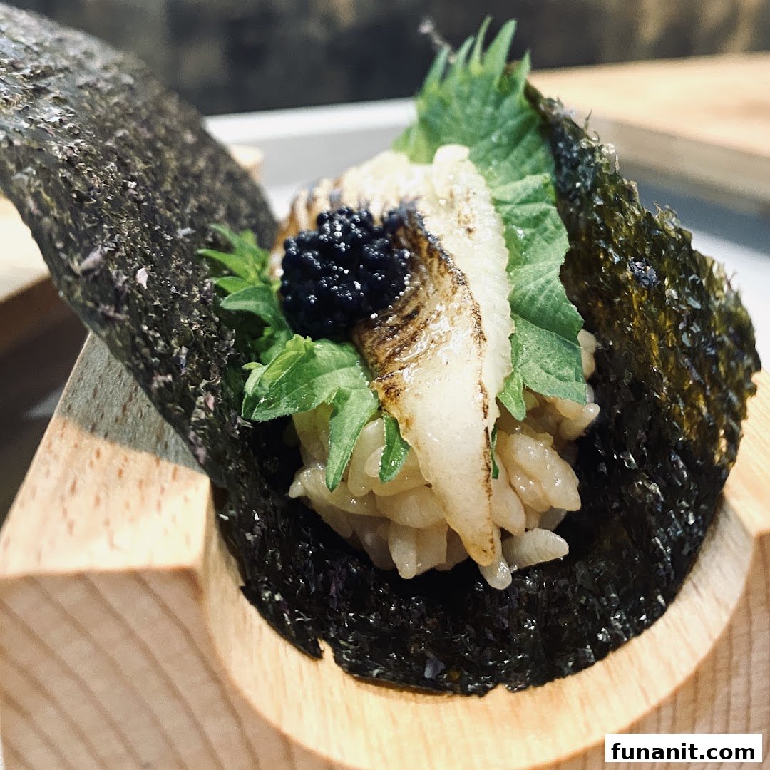 A close-up of a gourmet sushi hand roll featuring seared fish, black roe, and fresh greens, served in a wooden holder.