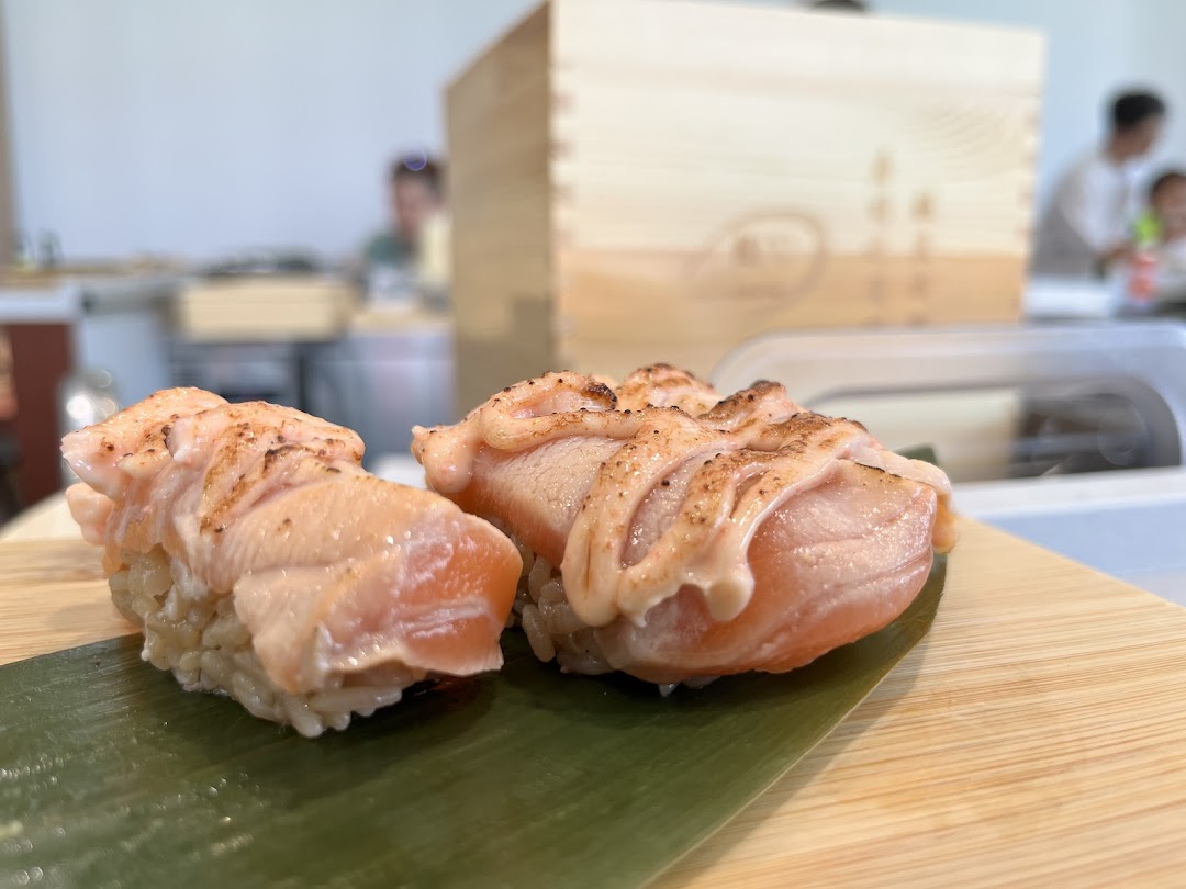 Two pieces of seared salmon sushi with sauce, served on a bamboo leaf and wooden board.