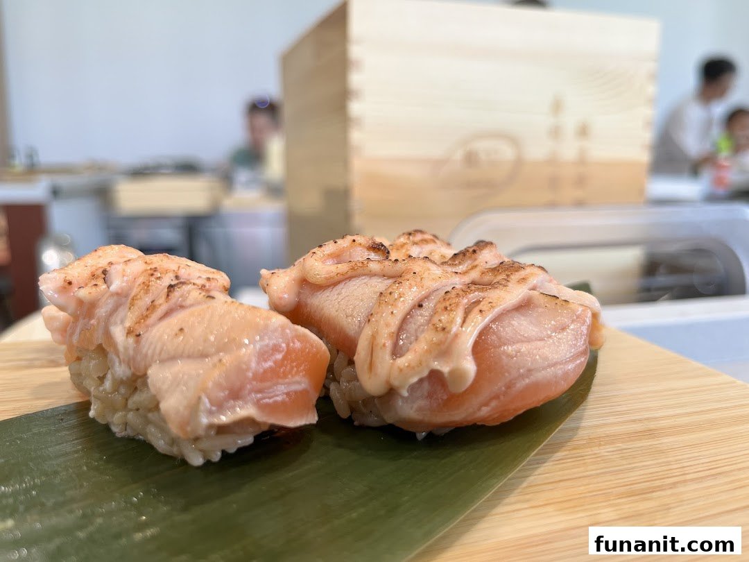 Two pieces of seared salmon sushi with sauce, served on a bamboo leaf and wooden board.
