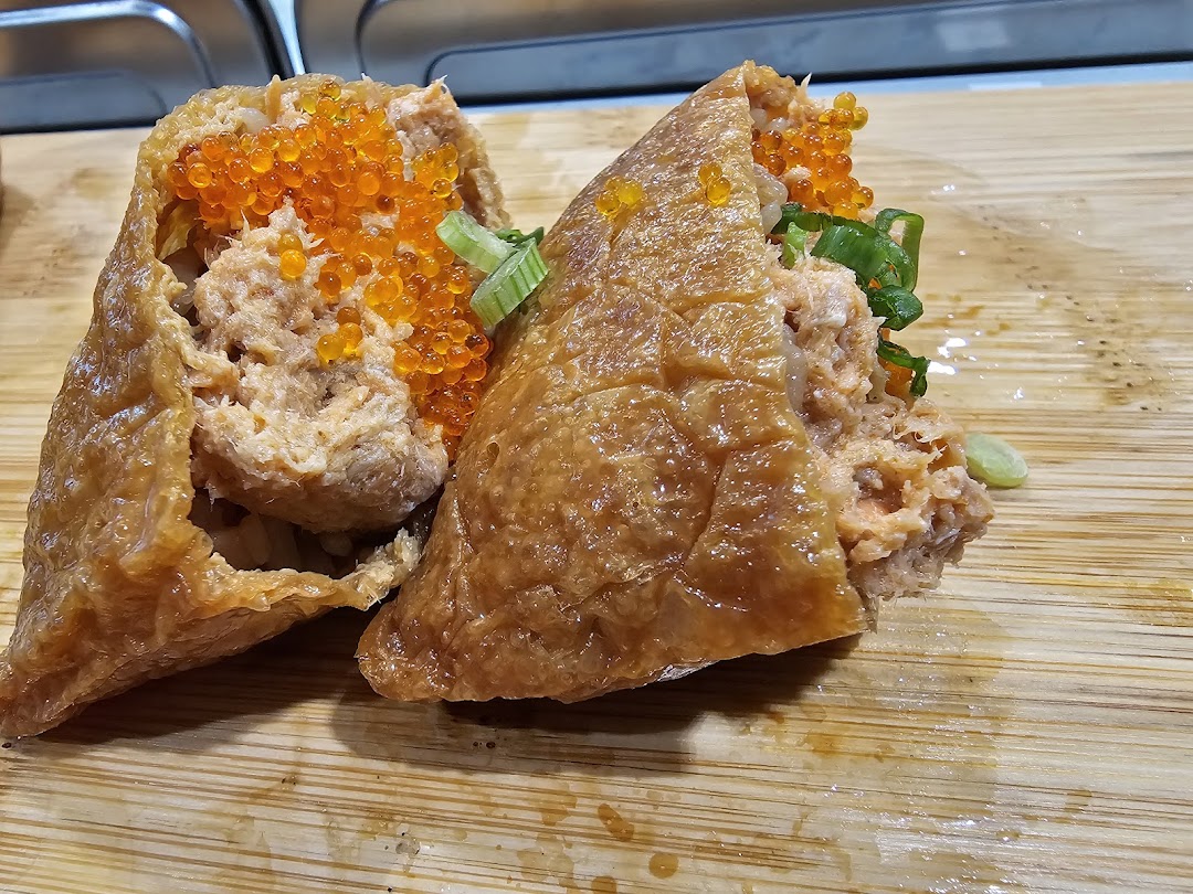 Two delicious inari sushi pieces filled with salmon, topped with vibrant orange roe and green onions on a wooden board.