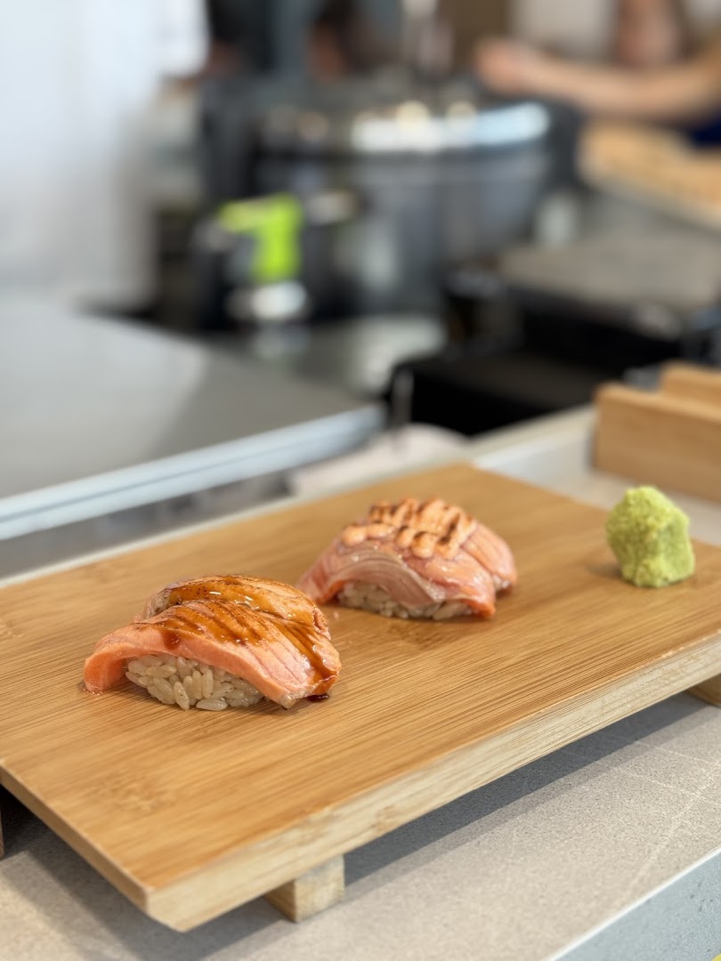 Two pieces of seared salmon sushi with wasabi on a wooden serving board, showcasing fresh ingredients.