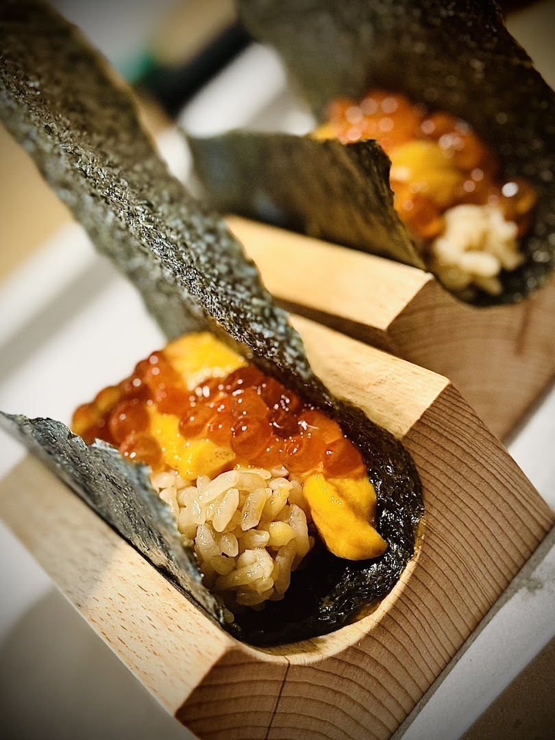 Two exquisite sushi hand rolls featuring fresh uni, glistening ikura, and rice, elegantly presented in wooden holders.