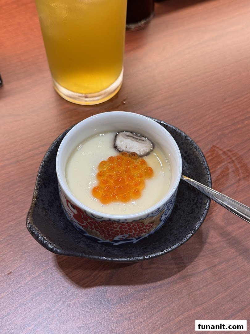 A close-up of a chawanmushi dish topped with salmon roe and mushroom, alongside a drink.