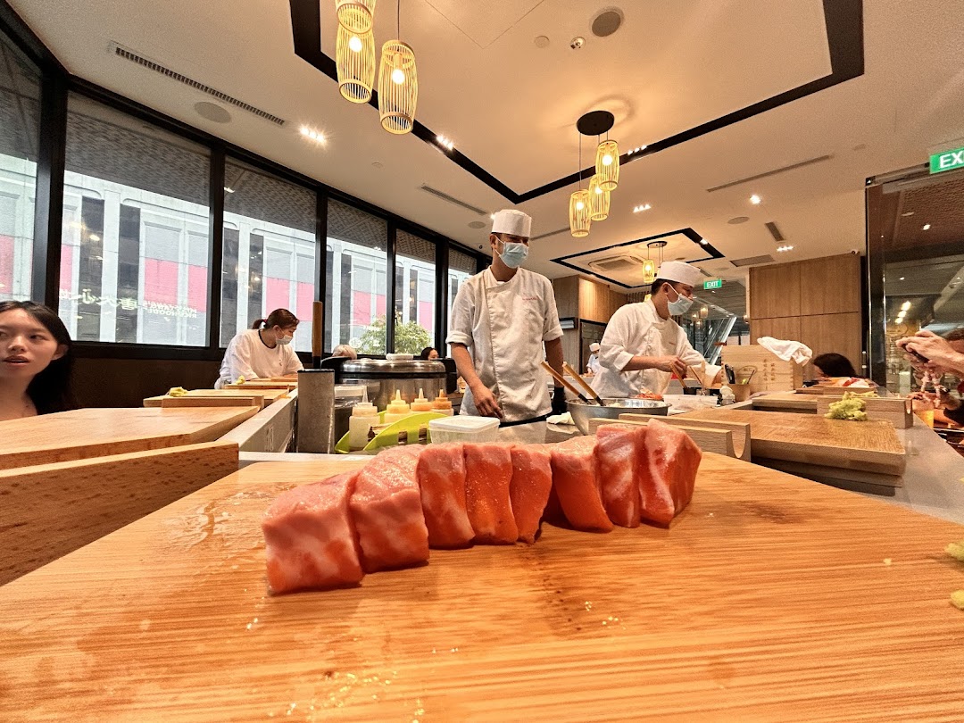 Chefs prepare fresh sushi at a counter, with large cuts of fish in the foreground at Sushi Zushi.