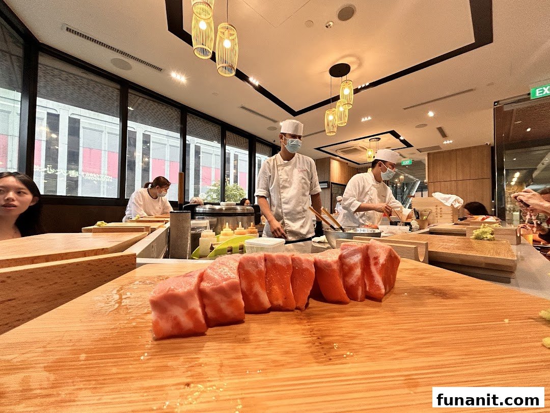Chefs prepare fresh sushi at a counter, with large cuts of fish in the foreground at Sushi Zushi.