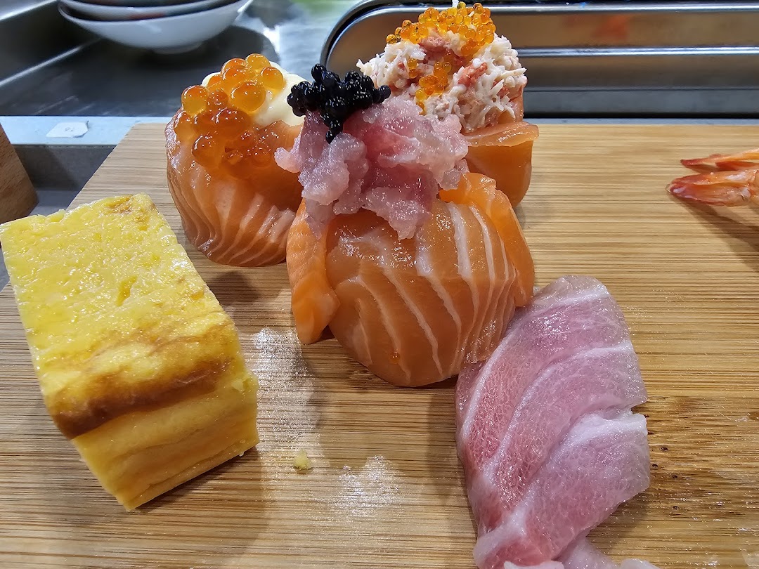 A close-up of fresh sushi and sashimi pieces, including salmon, tuna, and tamagoyaki, on a wooden board.