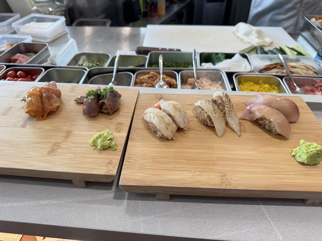 Freshly prepared sushi and sashimi on wooden boards at a sushi counter with ingredients in the background.