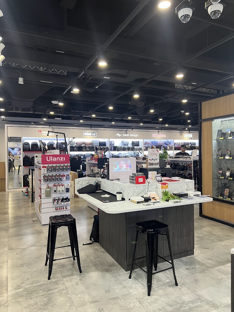 An interior view of T K Foto Technic, showcasing camera bags, accessories, and a central display counter with stools.