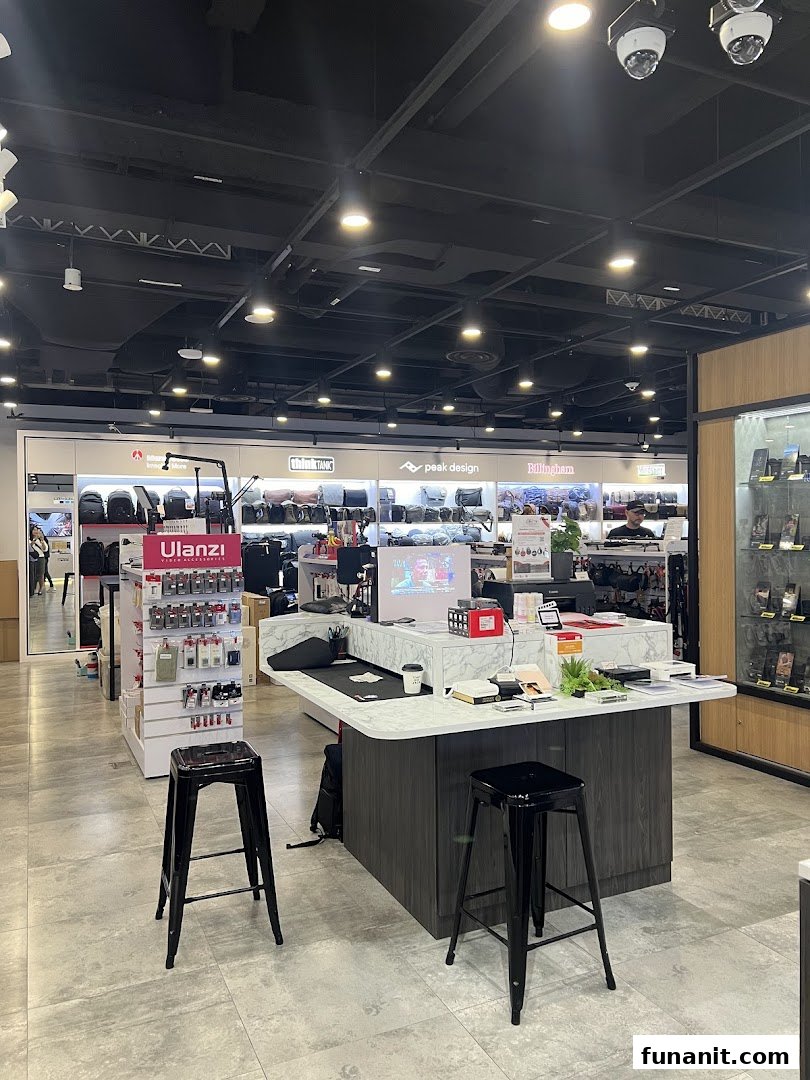 An interior view of T K Foto Technic, showcasing camera bags, accessories, and a central display counter with stools.