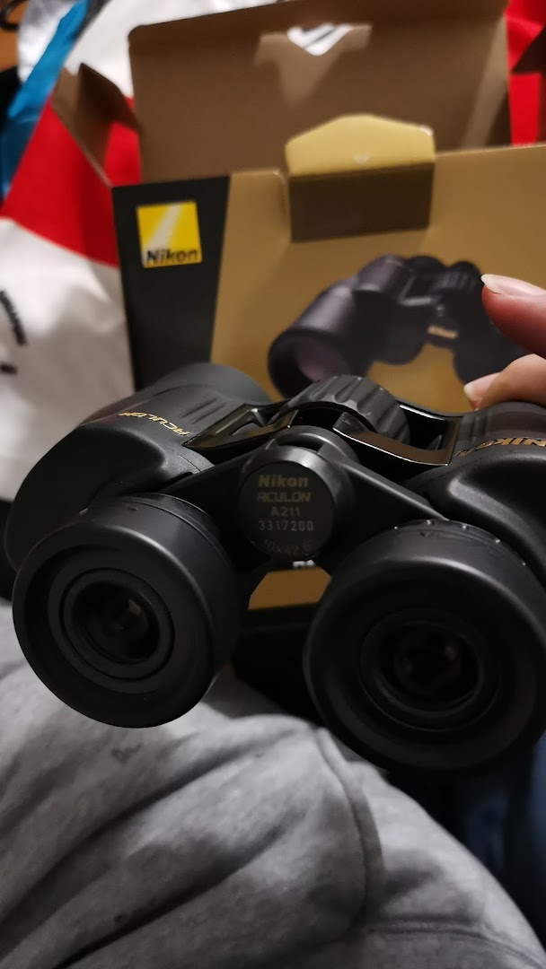 A pair of Nikon Aculon A211 binoculars held, with its product box visible in the background.
