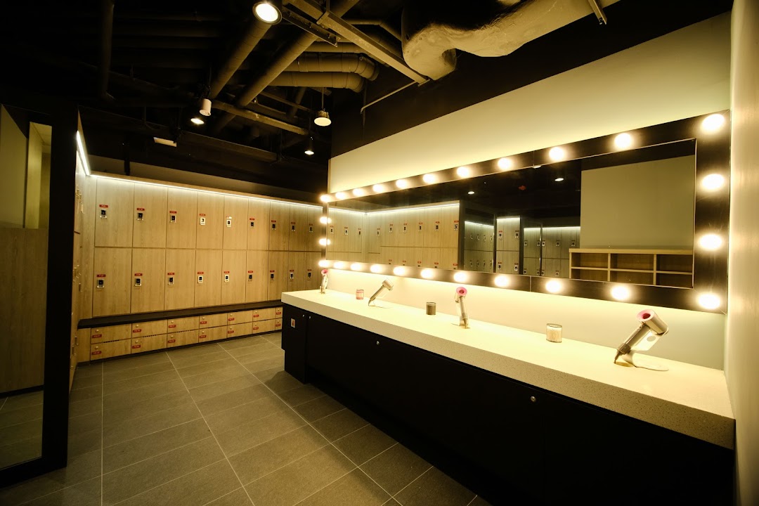 A modern and well-lit fitness center changing room featuring lockers, a vanity mirror, and Dyson hair dryers.
