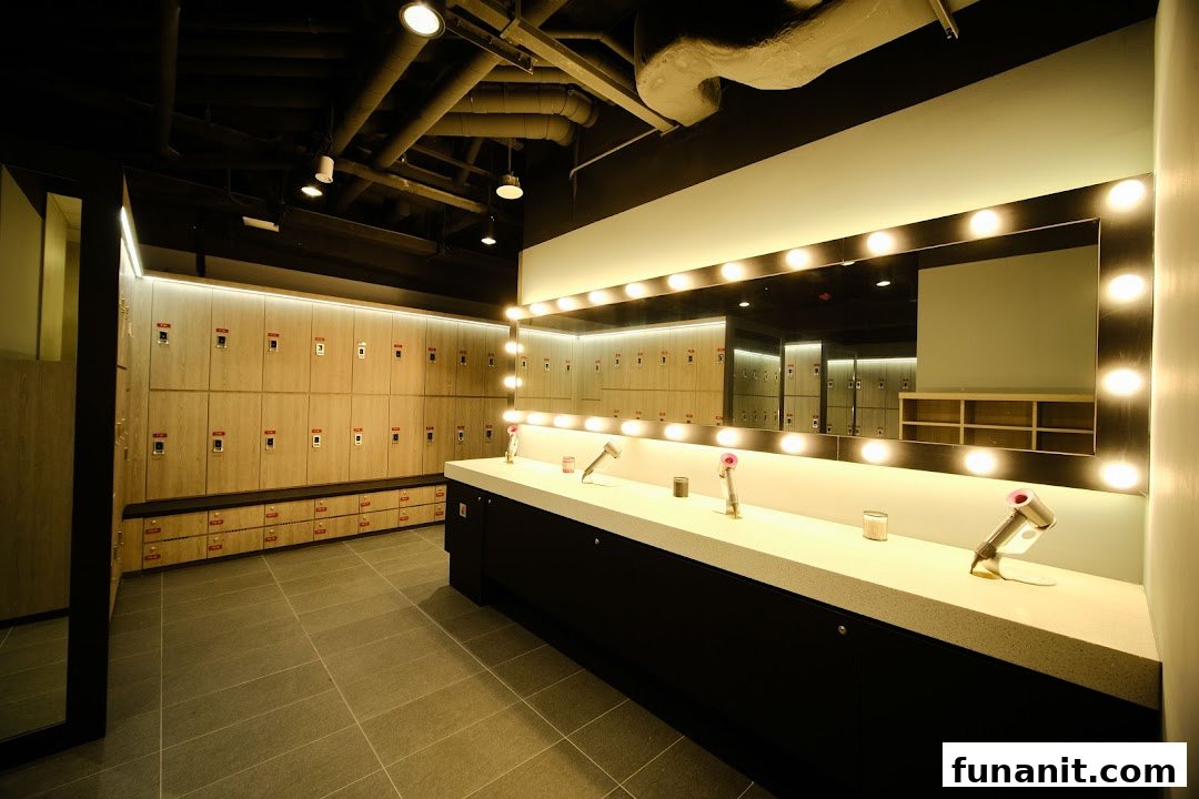 A modern and well-lit fitness center changing room featuring lockers, a vanity mirror, and Dyson hair dryers.