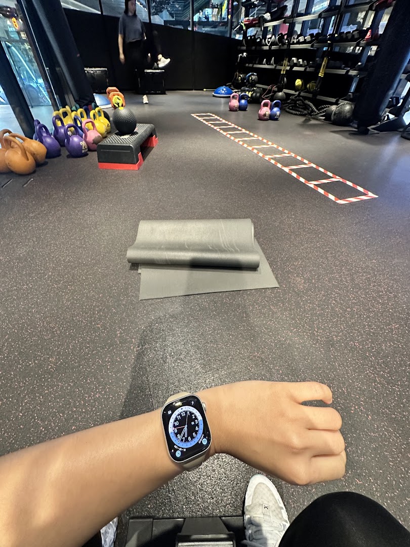 Interior view of a gym floor with fitness equipment, a yoga mat, and a person's arm wearing a smartwatch.