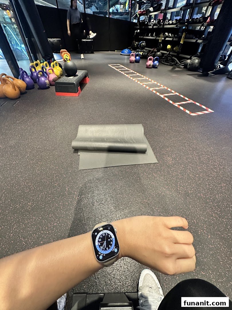 Interior view of a gym floor with fitness equipment, a yoga mat, and a person's arm wearing a smartwatch.