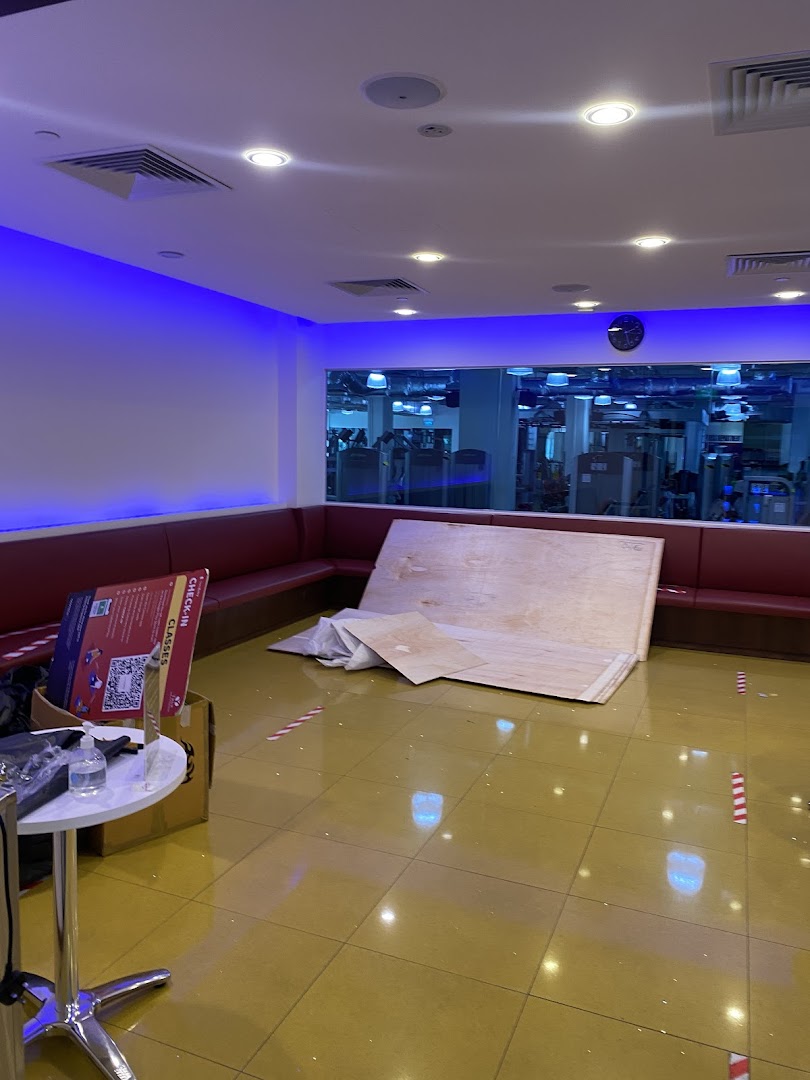 A modern lounge area with red seating and blue lighting, overlooking a gym, with some construction materials.