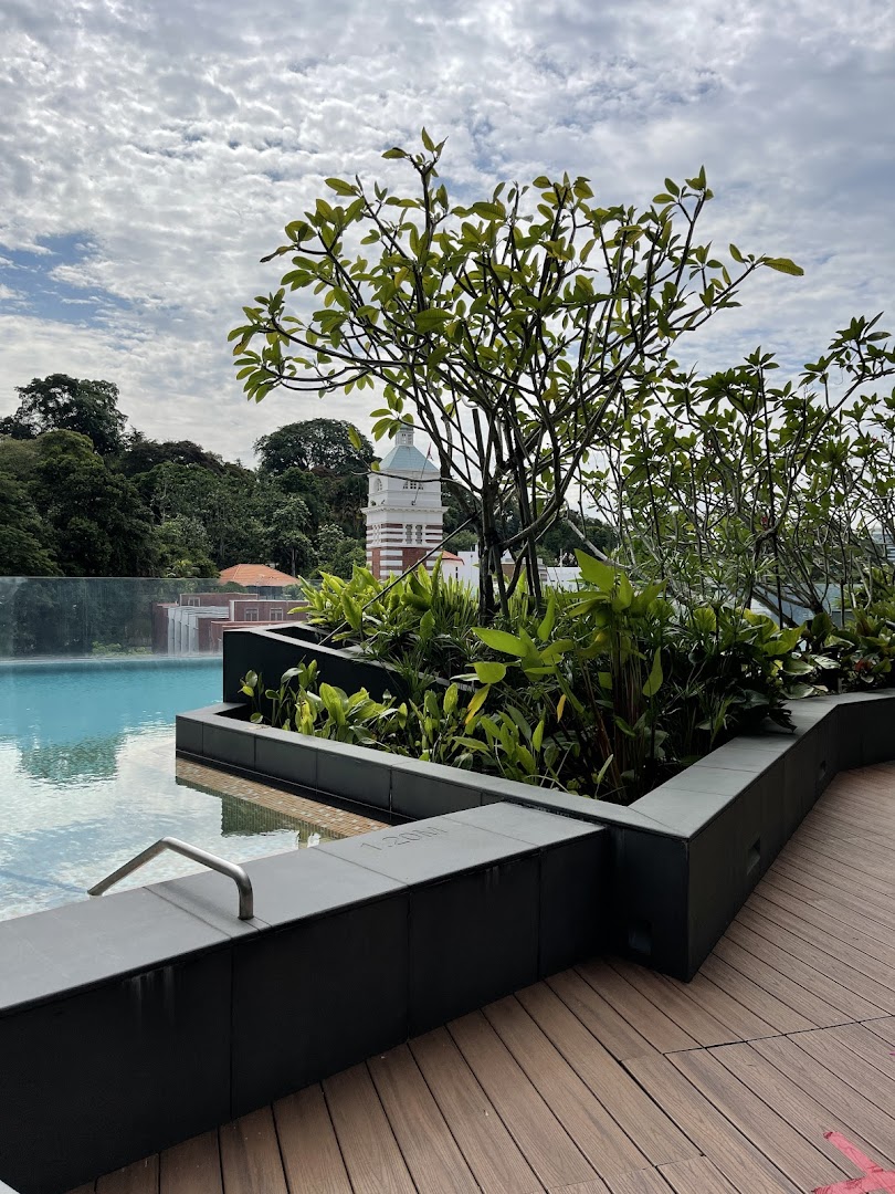 An outdoor pool area with lush greenery, wooden decking, and a view of a historic building under a cloudy sky.