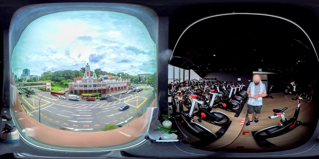 A panoramic view inside TFX Fitness Funan, showing spin bikes, a person, and a city landscape outside.