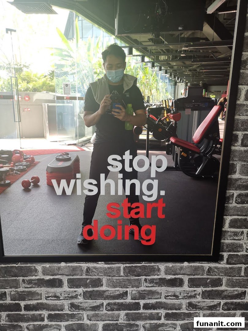 A person reflected in a gym mirror with motivational text 'stop wishing. start doing' and fitness equipment.