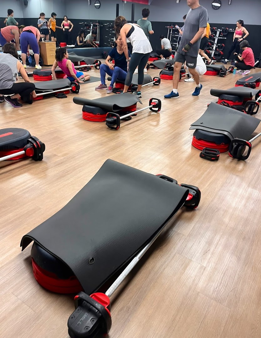 People exercising in a fitness studio with various equipment like steps and barbells.