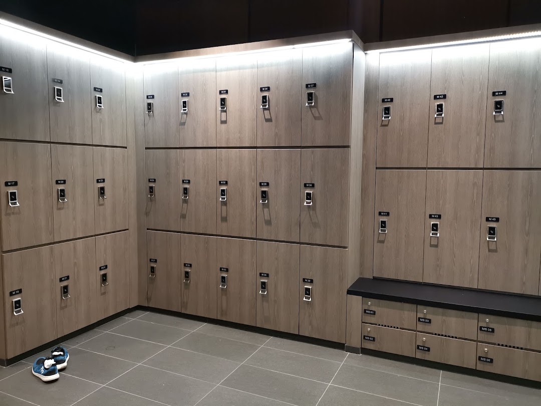 A modern, well-lit locker room with numerous wooden lockers and a bench at TFX Fitness.