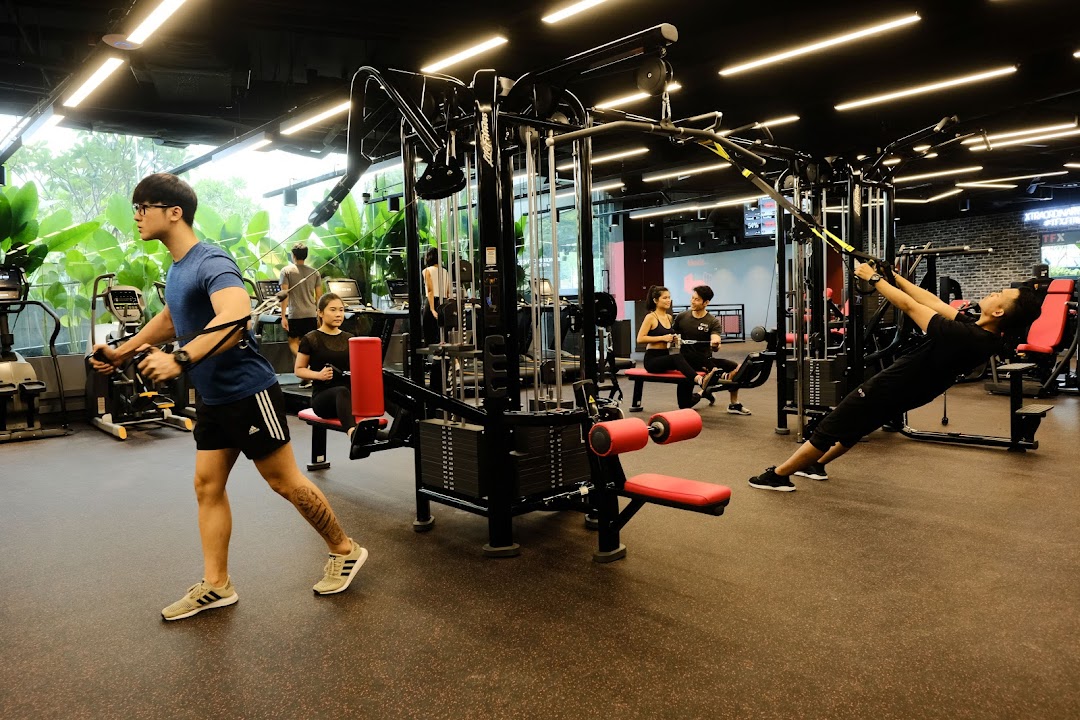 People are actively exercising with various equipment in a spacious, modern gym with large windows.