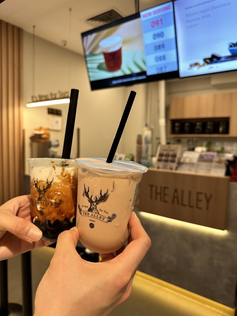 Two hands hold two signature bubble tea drinks from The Alley inside the vibrant shop.